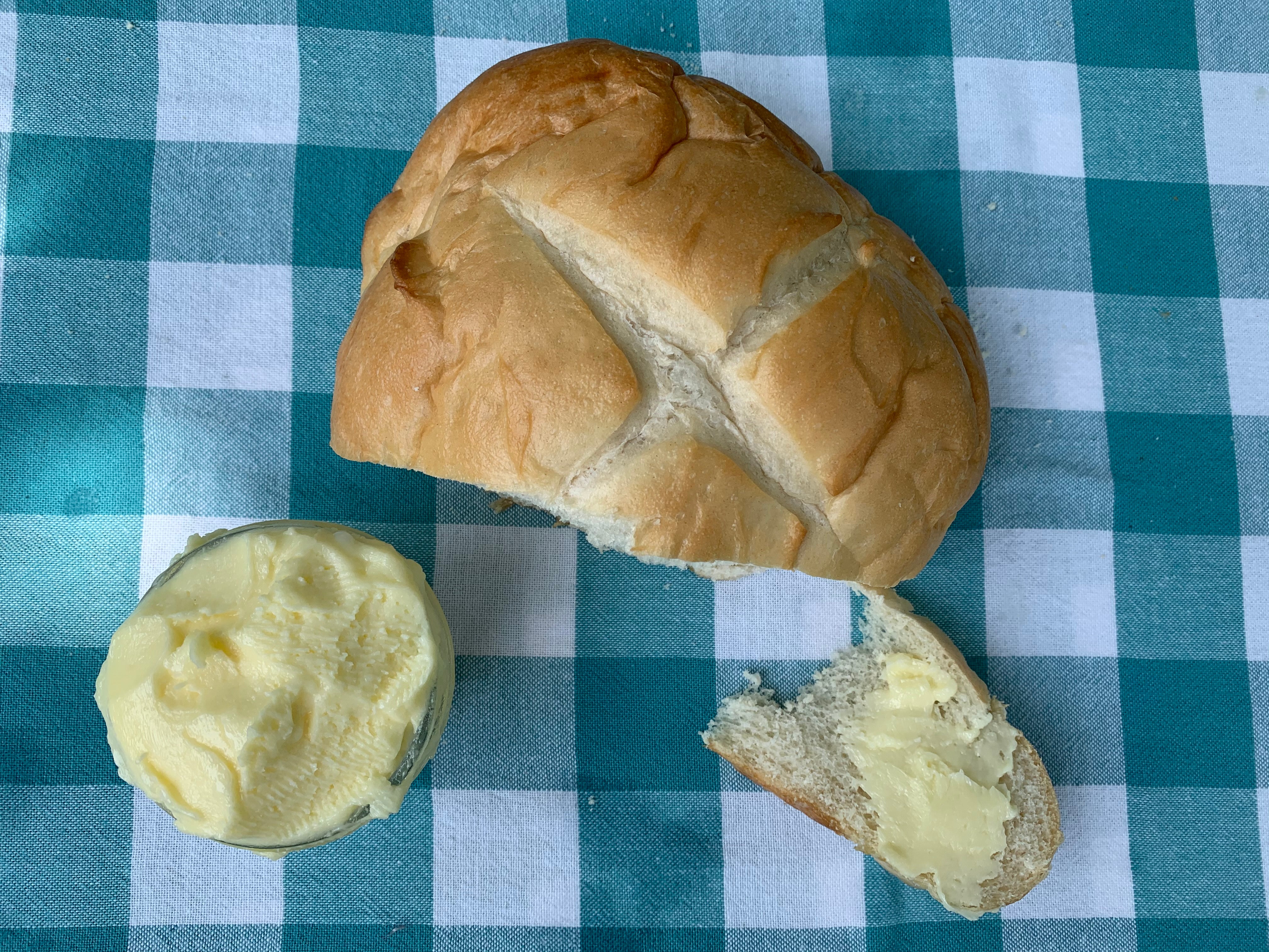 A loaf of bread on a table with a container of butter and a piece of bread off to the side with butter on it